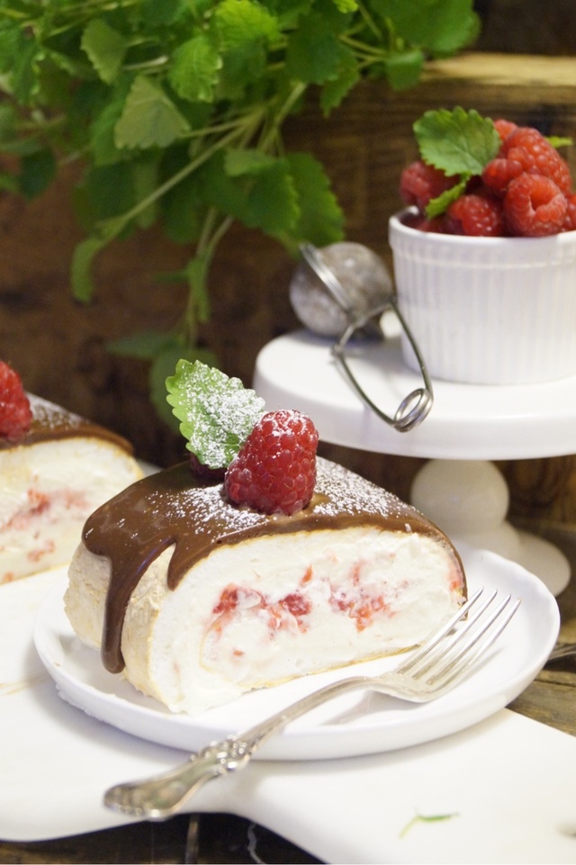 Pavlova-Rulltårta med hallon och vaniljswirl toppad med mjölkchoklad-ganasch.